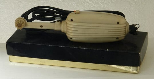 A very old electric toothbrush. The circular brush head is familiar, however the handle is big and bulky. The cable can be seen behind it.