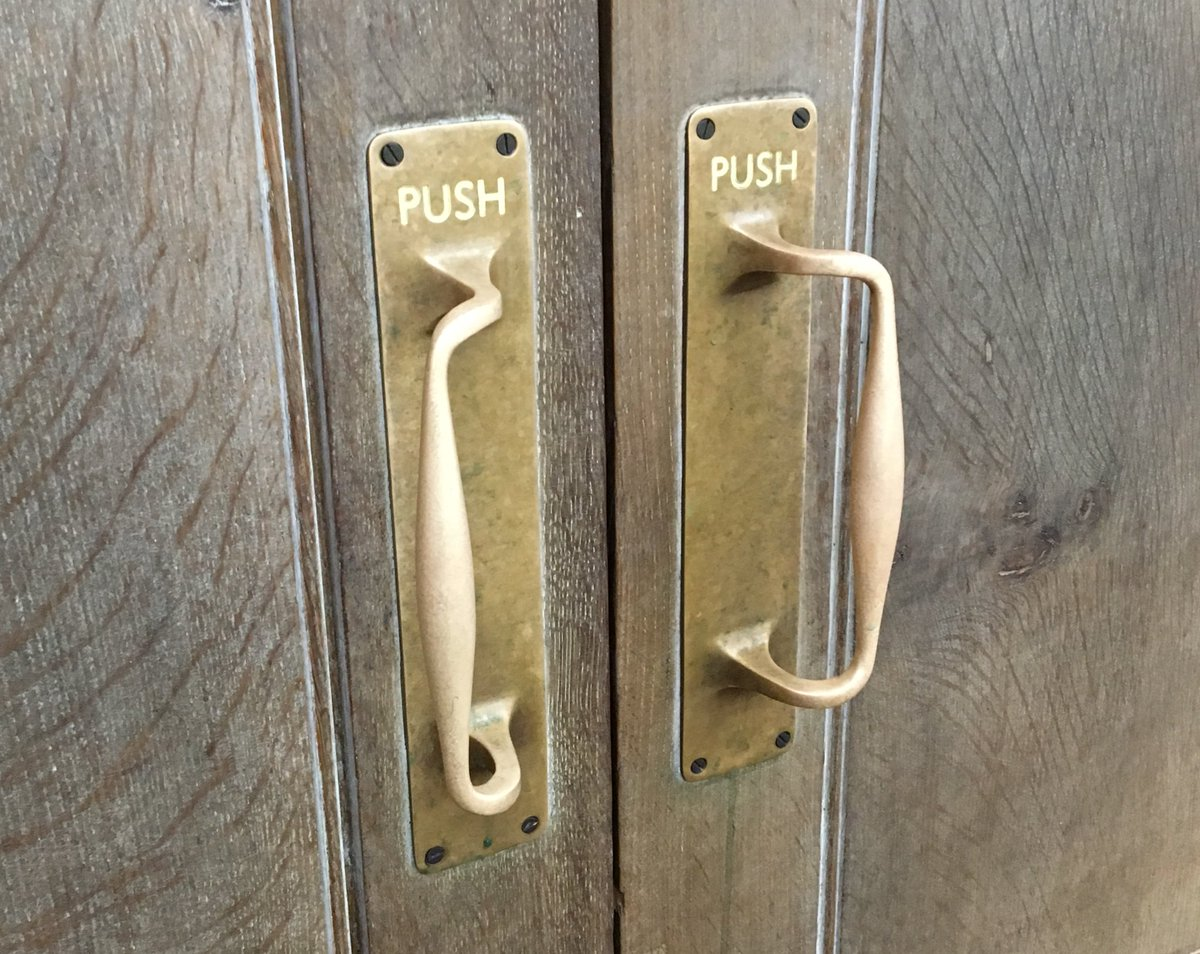 A close up shot of a set of brass door handles on a wooden door with the inscription "PUSH" above them.